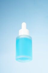 blue unbranded dropper bottle on glass against blue background. Skin care product presentation. Trendy showcase . bottom view