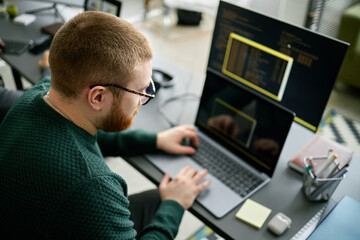 Coder working on project with two monitors and a laptop, immersed in code. Office environment...