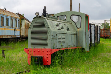 Vintage small diesel locomotive on a railway siding, surrounded by tall grass and old train cars....