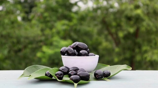 Closeup of Malabar Plum or Syzygium Cumini Isolated on in a White Bowl with Leaves on Wooden Table, Also Known as Java Plum, Jamun, Black Plum or Jambolan