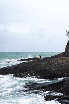 Side view of man with surfboard standing by rock