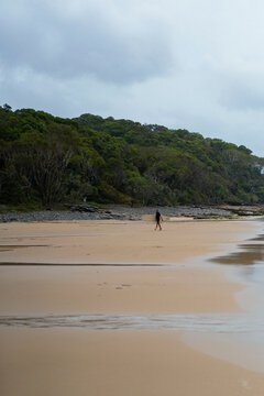 A middle aged man walks towards the beach with a surfboard