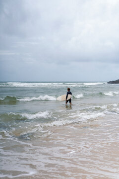 A middle aged man walks towards the beach with a surfboard