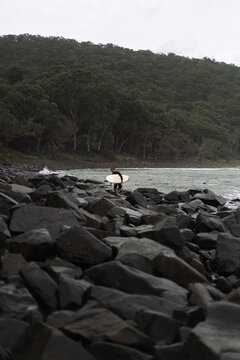 Man carrying surfboard while walking on rock