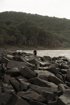 Man carrying surfboard while walking on rock