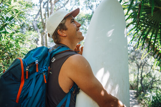 Smiling surfer holding board on lush tropical path