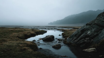 Fototapeta premium Misty Creek Landscape: Serene Waters, Dark Rocks, and Foggy Hills