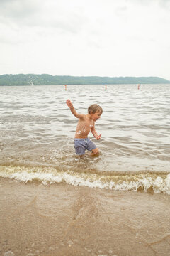 Young boy splashing in lake water near sandy shore.Keywords: