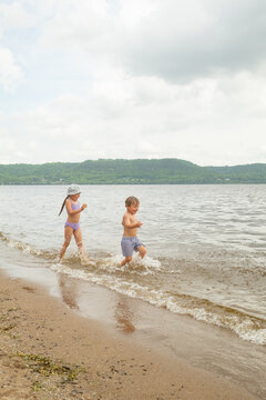 Young boy splashing in lake water near sandy shore.Keywords: