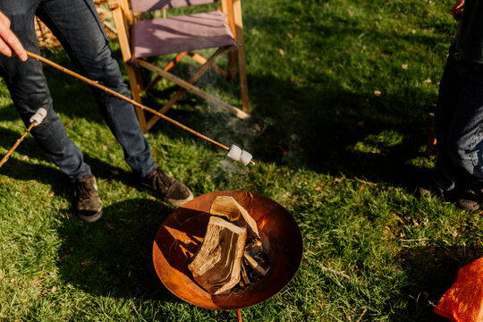 Person roasting marshmallow over a backyard fire pit in sunlight