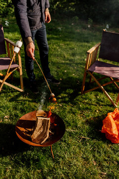 Person roasting marshmallow over a backyard fire pit in sunlight