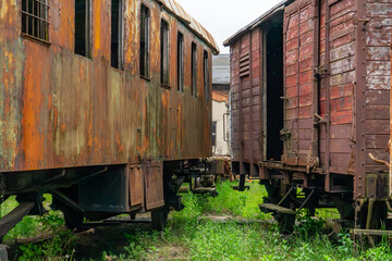 Old railway cars standing on a siding, covered with rusty metal and weathered wood. Visible signs...
