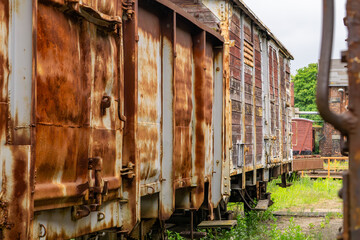 row of old, rusty freight train cars standing on a railway siding. Heavy corrosion and peeling...