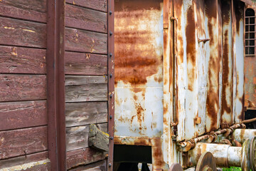 fragment of old railway cars – one made of weathered wood, the other of heavily rusted metal. The contrast of materials and colors highlights their age and deterioration. The scene captures the passag