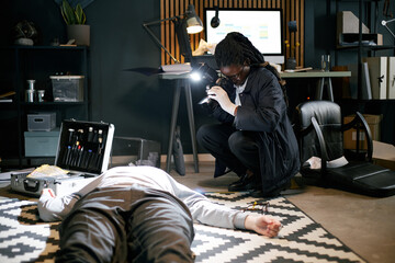Forensic investigator examining crime scene and collecting evidence while crouching by body....