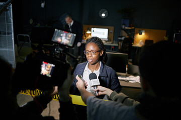 Interviewer speaking to a journalist in a busy newsroom with reporters and cameras around, creating dynamic atmosphere for media coverage on current events in modern office environment