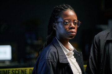 Crime scene investigator examining a scene under intense lighting, focused on gathering evidence. Investigator wearing glasses and a dark jacket, capturing the details of critical work