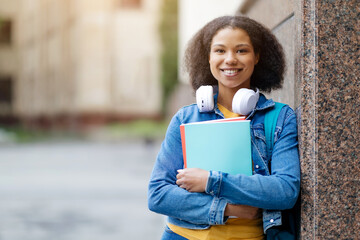 Black African American female student standing against a marble wall outdoors at campus, holding...