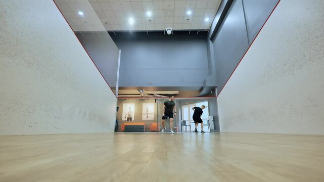 Intense indoor squash game with low angle showing footwork and momentum