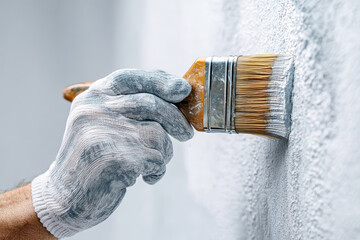 Close-up of a gloved hand using a paintbrush to apply paint at a construction site