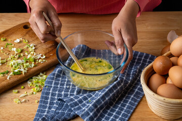 person is beating raw eggs with spring onions with wooden chopsticks