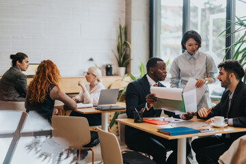 Team members at a co working space discussing ideas and documents, with natural lighting and a...