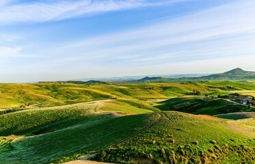 beautiful green ristic landscape of spring hills with grassland fields covered with young fresh grass and countryside road leading to a cloudy sunset