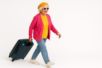 Stylish senior woman walking with suitcase on white background – fun travel concept