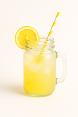 Glass mason jar of lemonade with lemon slice and striped straw – summer drink on white background