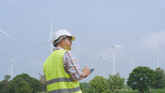 Engineer working with laptop at wind turbine field generating electricity for renewable clean energy
