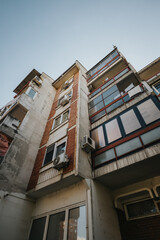 A photograph showing an urban apartment building with brick and concrete walls, balconies, and visible air conditioners, representing old architecture and city living.