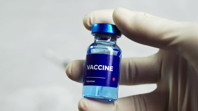 a doctor checks the vaccine liquid in a vial and shows it to the camera. health and medical concepts.