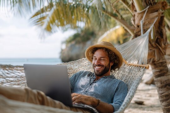 Enjoying remote work bliss on a tropical beach under a palm tree while relaxing in a hammock with a laptop and a straw hat