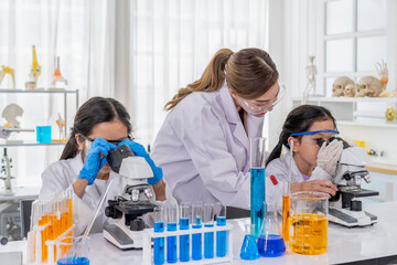young female teacher helps kid to conduct chemical experiment with microscope,primary school...