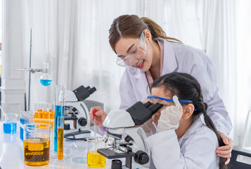young female teacher helps kid to conduct chemical experiment with microscope,primary school...