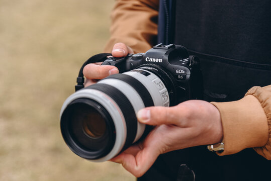 ST.PETERSBURG, RUSSIA - MAY 10, 2025 Canon EOS R6, black and white dslr camera in hands, large long lens, young caucasian man photographer at work outdoors in sunny summer day