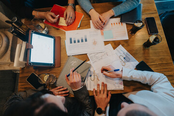 A team of individuals engaged in a collaborative discussion involving paperwork, graphs, and digital technology to strategize and succeed in their work goals.