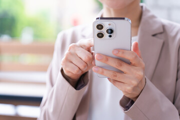 コーヒーを飲みながらスマートフォンを操作している若い女性　ビジネスイメージ	