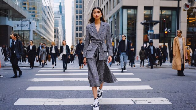 Stylish model wearing a gray blazer and skirt walks confidently across a busy new york city crosswalk, showcasing urban fashion trends amidst the bustling crowd - Powered by Adobe