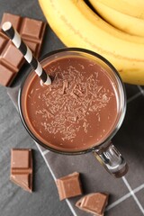 Tasty chocolate milk in glass cup, pieces and bananas on black table, flat lay