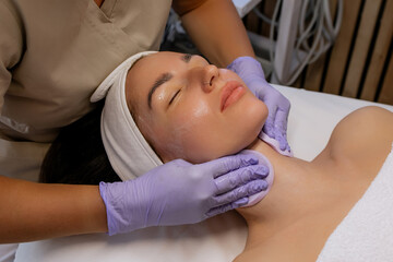 Close-up of professional esthetician performing a facial treatment with cotton pad on woman’s neck during beauty session at a spa, skincare procedure