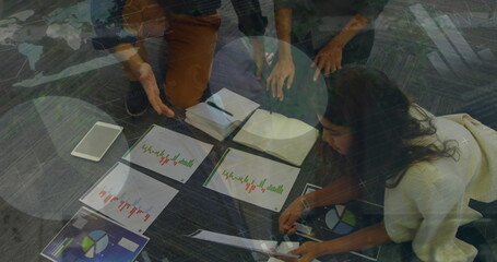 Kneeling colleagues leaning over printed charts on carpeted office floor, with tablet and notebooks