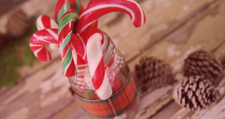 Showcasing glass jar with plaid ribbon holding candy canes on rustic tabletop with pinecones