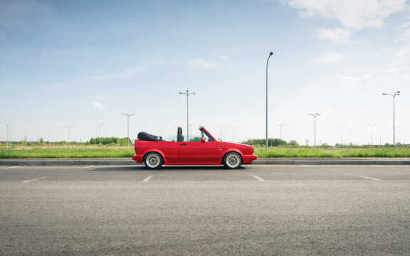 Side profile view of classic Volkswagen Golf cabriolet. Red VW golf mk1 in big empty parking lot in countryside, clean sky in the background. Lviv, Ukraine - May 02 2014