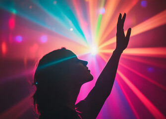 Silhouette of a woman with her hand raised in a vibrant, colorful, light filled space.