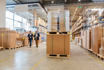 Employees meeting in a large warehouse with stacked pallets and boxes