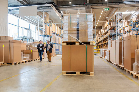 Employees meeting in a large warehouse with stacked pallets and boxes