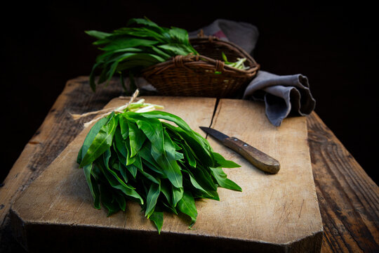 Bundle of wild garlic on a rustic cutting board with a knife and willow basket
