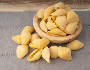 Raw conchiglioni pasta in wood bowl. Dry conchiglie noodle in shell shape