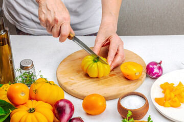 A woman is preparing a tomato salad. Ripe vegetables, herbs, aromatic spices, olive oil